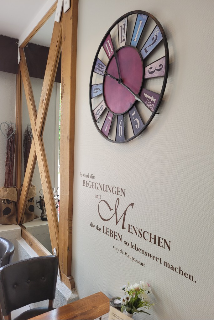 Eine Wand mit einer Uhr darunter ein Zitat von Guy de Maupassant: Es sind die Begegnungen mit Menschen, die das Leben so lebenswert machen.