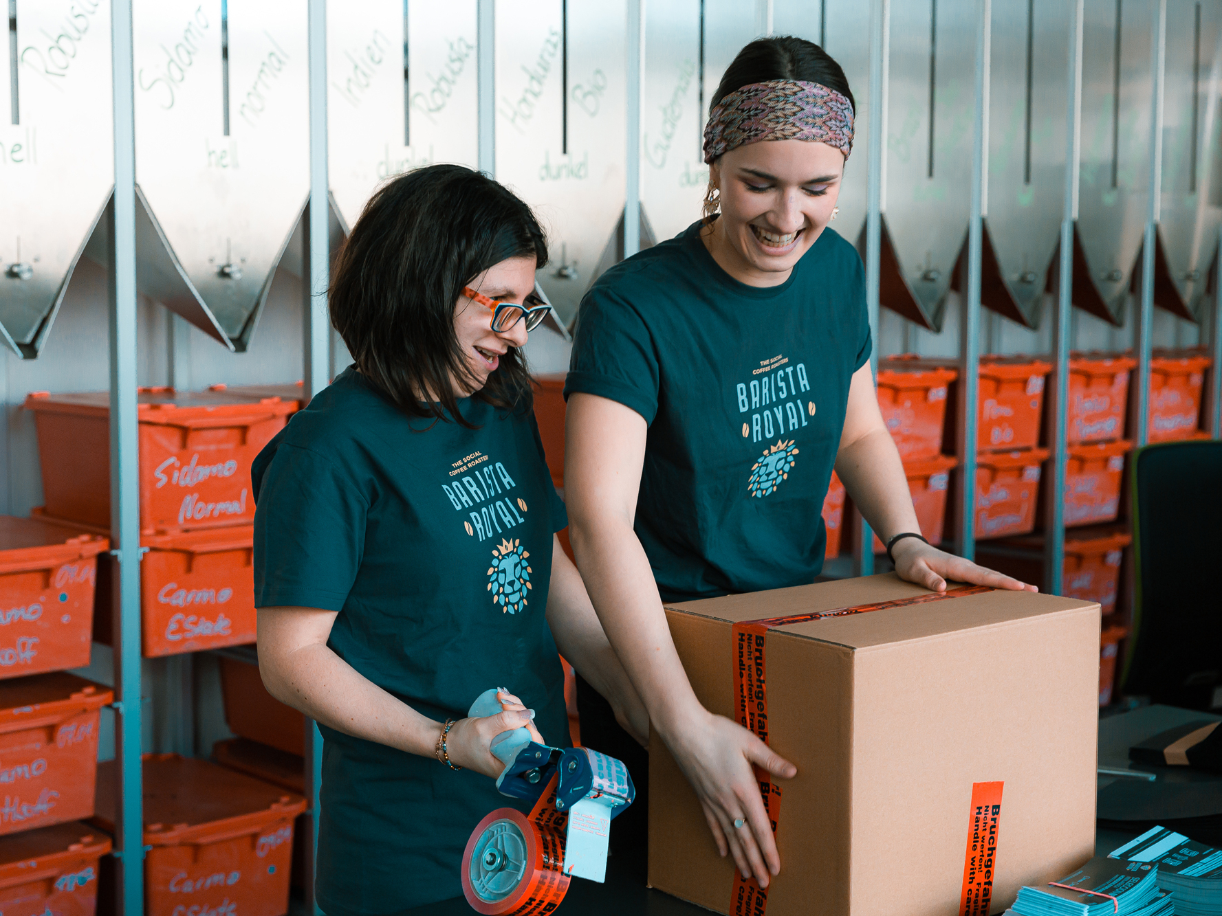 Eine Rösterin und ein Teammitglied mit Behinderung beim Verpacken von Bestellungen.