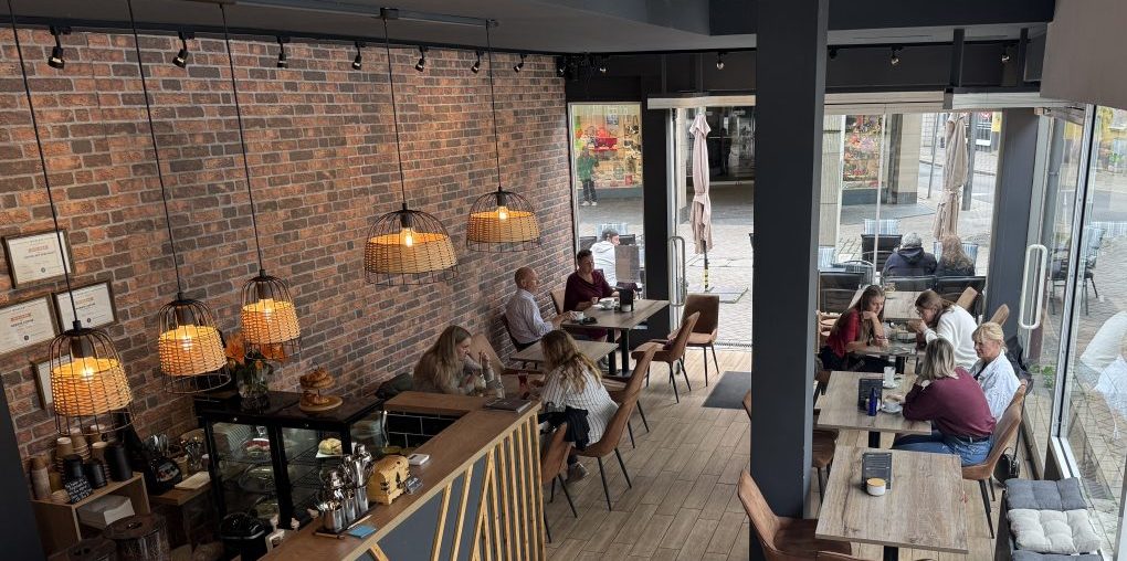 Das Bild zeigt das Café Il Barista Tommy Dee. Man sieht einen Teil der Theke und einige belegte und freie Sitzplätze im Erdgeschoss.