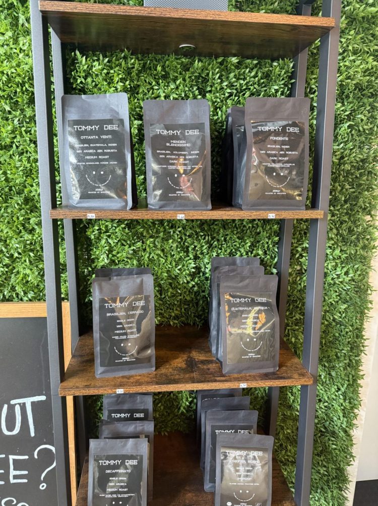 Das Bild zeigt ein Regal in dem Café Il Barista Tommy Dee in dem mehrere 250g große Packungen Kaffee stehen. Die Packungen sind schwarz und enthalten verschiedene Röstungen.